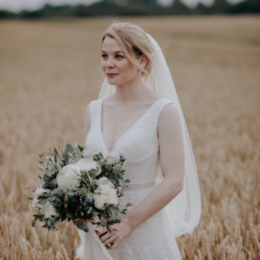 Bride standing in wheat field with white bridal bouquet