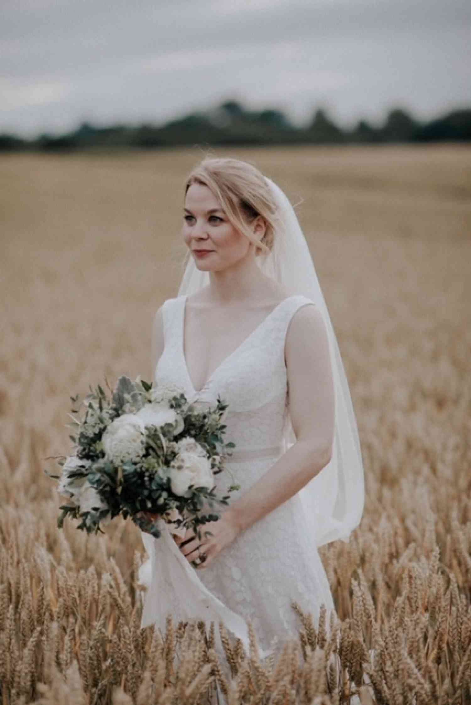 Bride standing in wheat field with white bridal bouquet